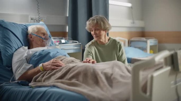 医院病房: 老人戴着氧气面罩躺在床上休息，有爱心的美丽妻子看望心爱的丈夫，支持他坐在旁边，手牵着手，