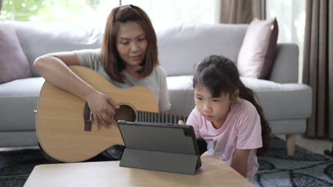 母亲弹吉他，女儿在数字平板电脑上观看和享受