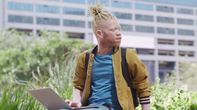 体贴的白化病非裔美国人，用笔记本电脑坐在公园里，留着辫子