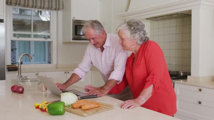 快乐的高加索高级夫妇在厨房准备饭前用笔记本电脑做食谱