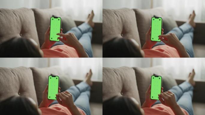 女人躺在沙发上，使用带有绿色模拟屏幕的智能手机