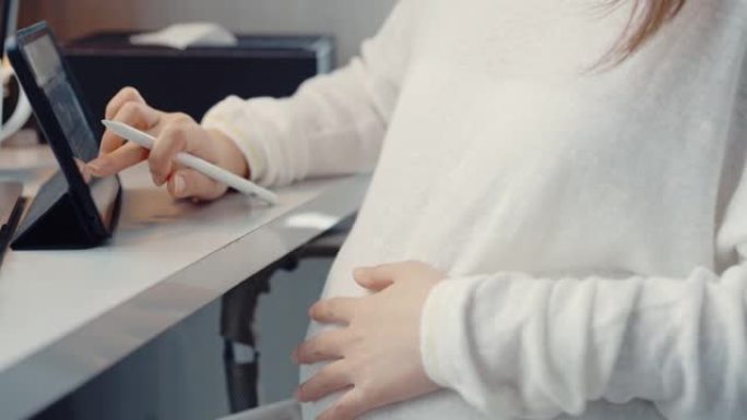 体贴的孕妇在数字平板电脑上写作。