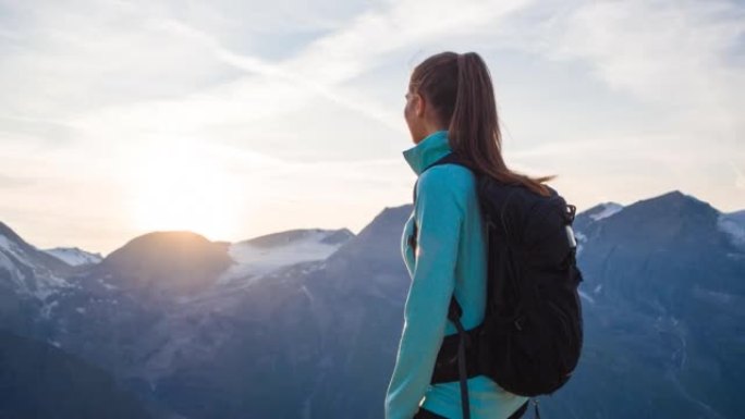 年轻的女徒步旅行者站在山顶上，在日落时欣赏壮丽的景色