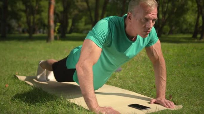 一位金发碧眼的健身教练正在公园里练习，用手机进行tabata训练，一会儿拿着木板