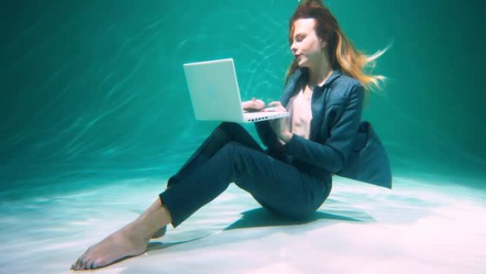 工作狂概念年轻快乐迷人的老板商务女性穿着正式西装使用笔记本电脑水下慢动作。