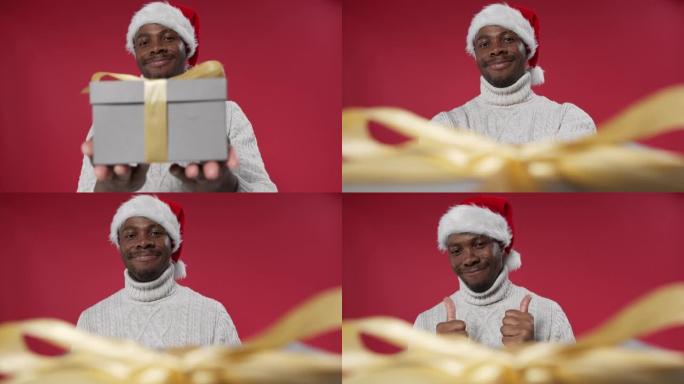 一个戴着圣诞帽和羊毛针织毛衣的黑皮肤男人微笑着，递给相机一个礼品盒