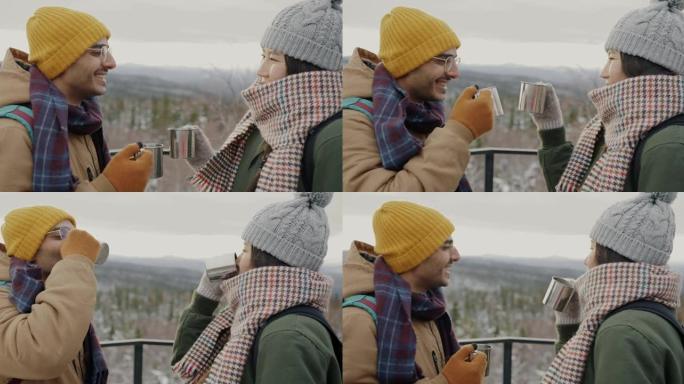 幸福的夫妇游客叮当作响的金属杯喝着大笑，看着令人惊叹的冬季风景