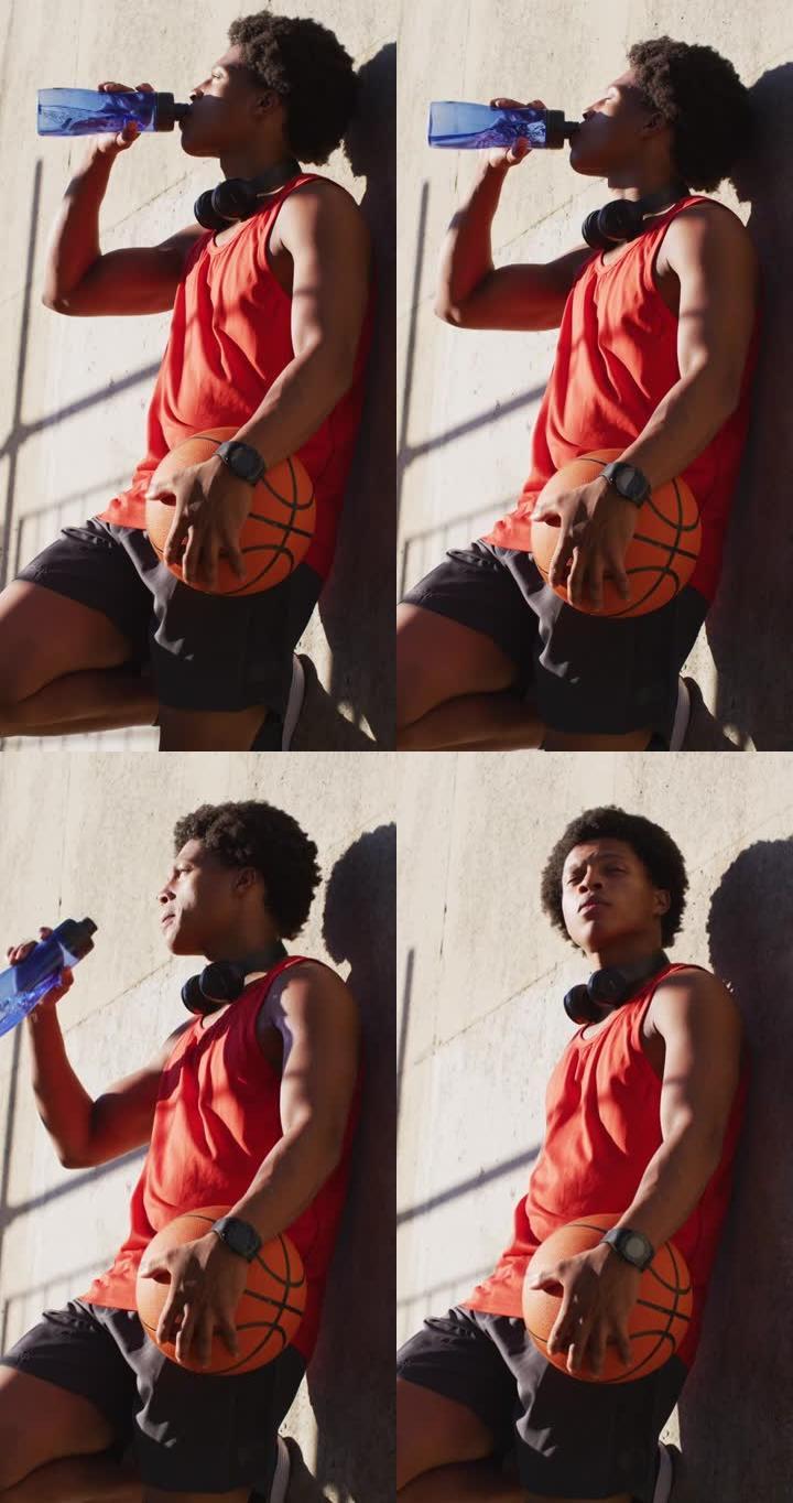 一个混血儿男子靠在墙上，喝水，拿着篮球的垂直射击