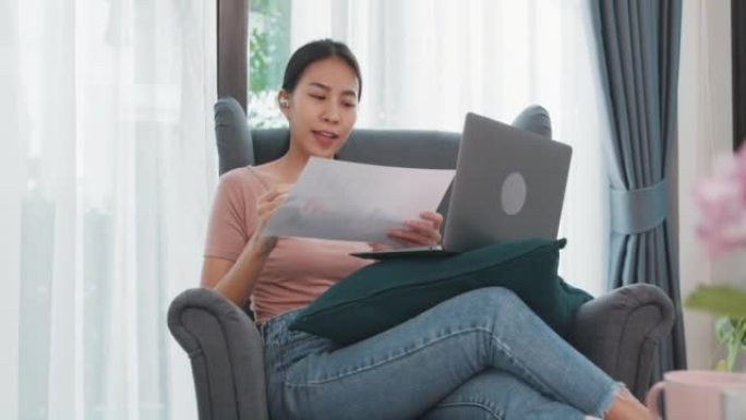 亚洲女商人在客厅在家工作时，使用笔记本电脑与同事讨论视频通话计划。