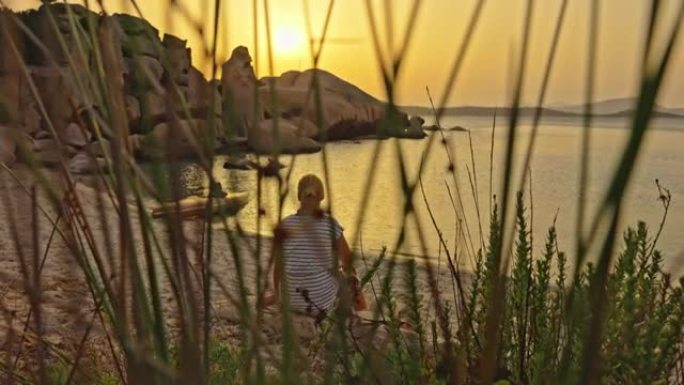 坐在海滩上的金发女孩的景色，撒丁岛，意大利。