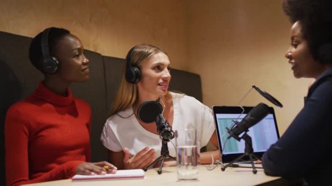 三位不同的女性广播主持人戴着耳机在广播播客上的麦克风上讲话