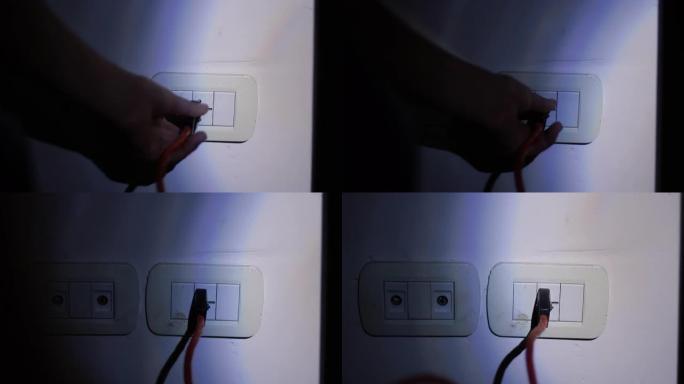 在停电或停电期间，在黑暗中使用手电筒在公寓墙壁上连接插座的男性手。特写。4k分辨率。