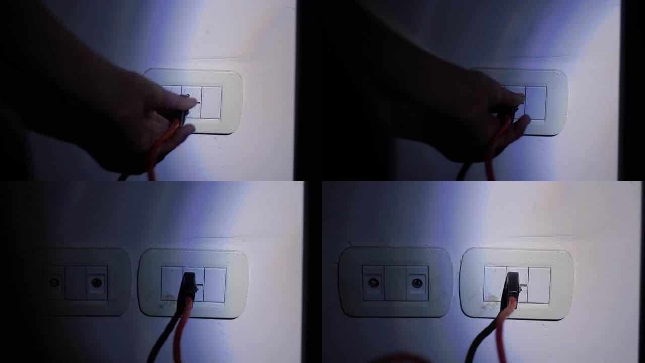 在停电或停电期间，在黑暗中使用手电筒在公寓墙壁上连接插座的男性手。特写。4k分辨率。