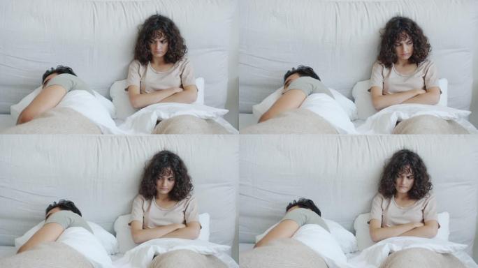 愤怒的白人妇女看着躺在床上的熟睡的丈夫阿拉伯男人