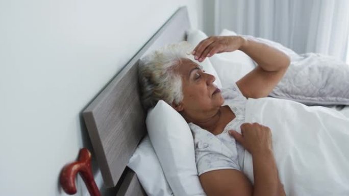生病的非洲裔美国高级妇女躺在家里的床上时抱着头