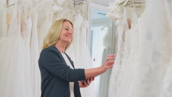 新娘商店的成熟女性老板拿着数码平板电脑在慢动作中翻阅婚纱