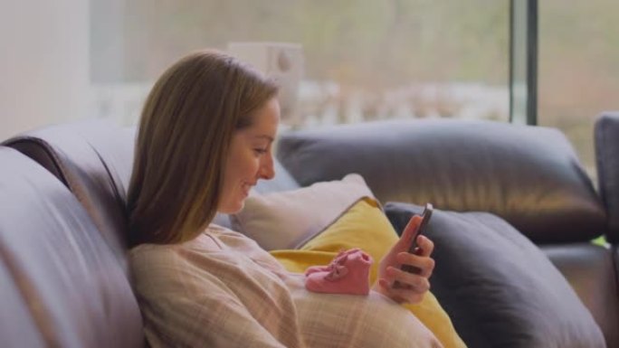 孕妇在家坐沙发用手机拍肚子上的小宝宝鞋自拍-慢动作拍