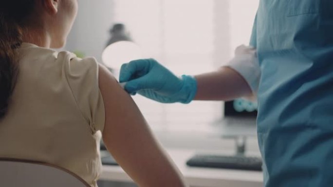 戴着手套的医生拿着带有疫苗的注射器，并在肩膀上注射患者