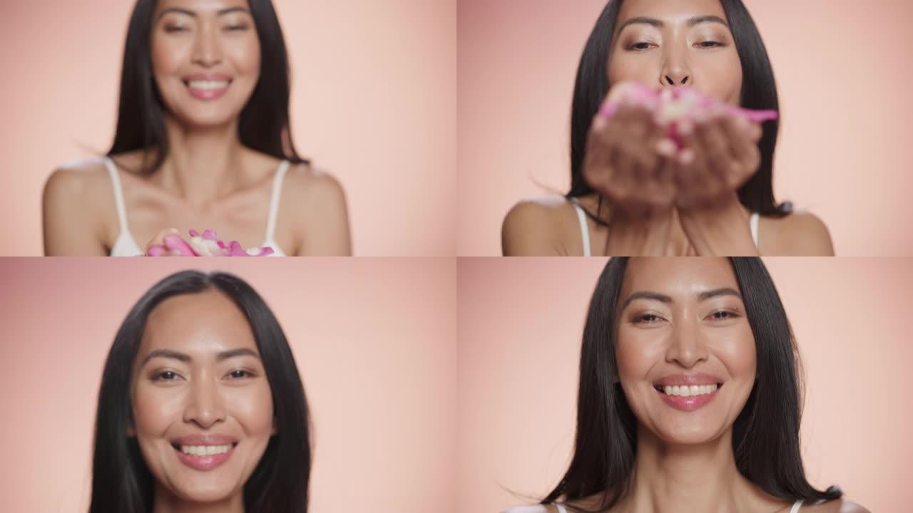 女性美女肖像。微笑的多民族亚洲黑发女人从她的手掌吹着粉红色的花瓣。柔软孤立背景下的健康、水疗和天然护