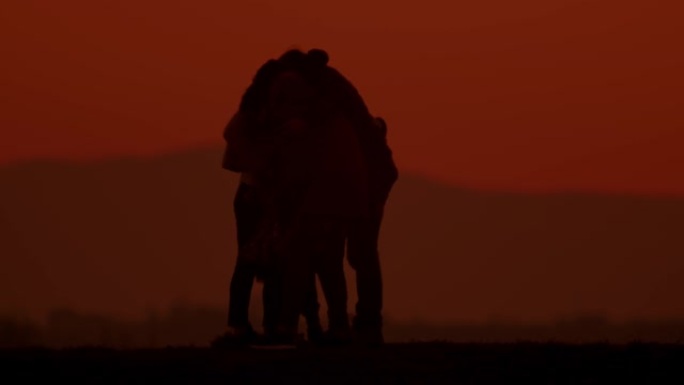 SLO MO在黄昏时拥抱在山上的剪影中充满爱心的家庭