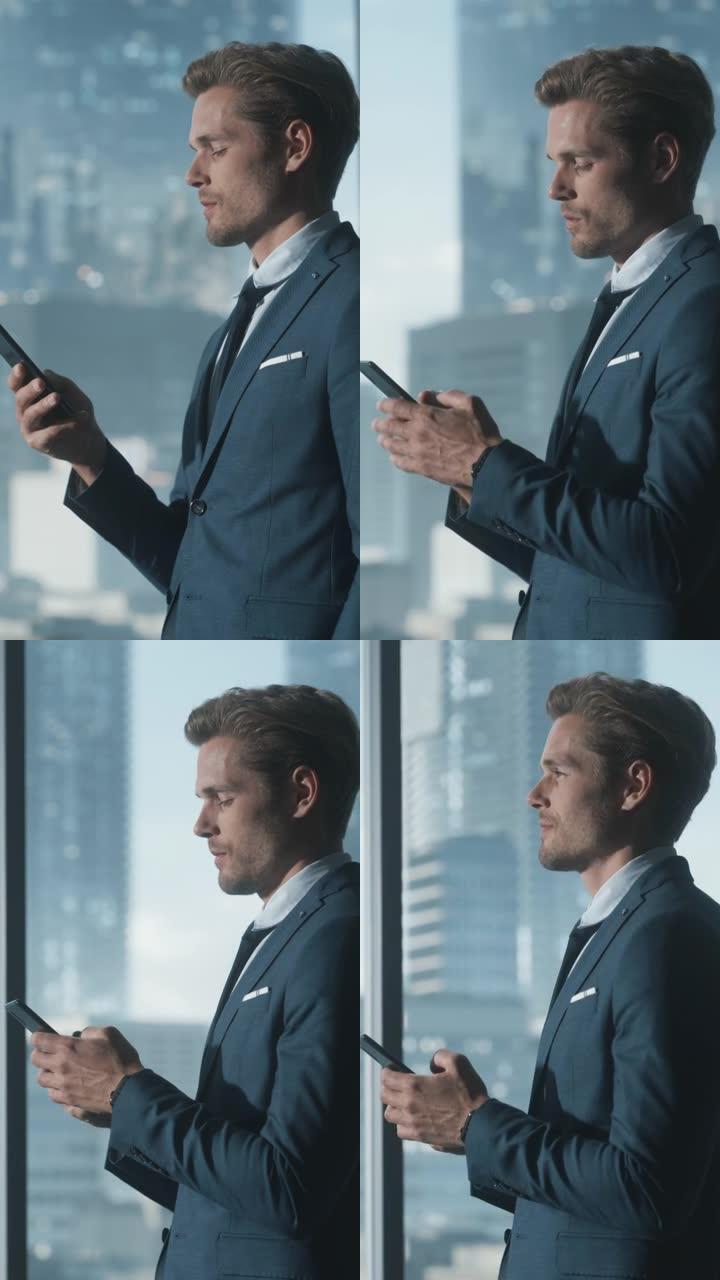 垂直屏幕: 自信的商人站在现代办公室的西装中，使用智能手机，看着窗外的摩天大楼。成功的财务经理计划工