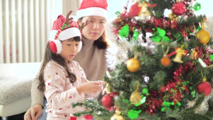 小女孩和母亲在圣诞节用装饰品装饰圣诞树