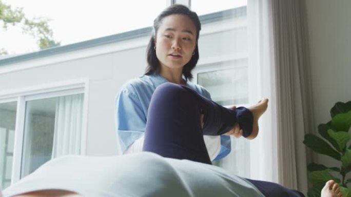 亚洲女性理疗师在手术中抱着女性患者的腿躺在检查床上