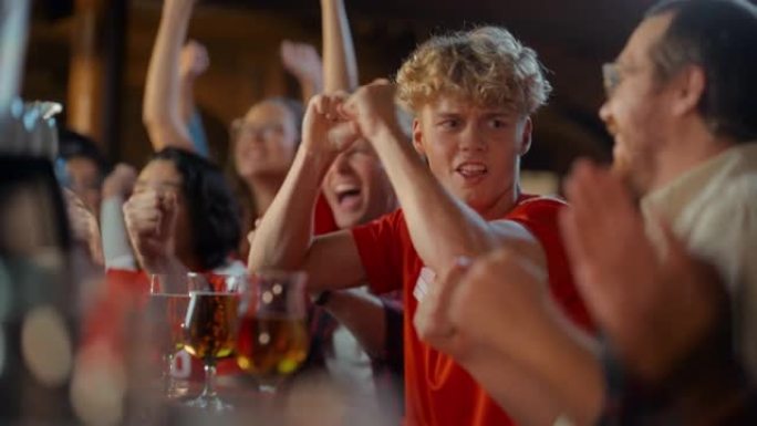 一群年轻朋友在体育酒吧观看电视直播足球比赛。激动的球迷欢呼雀跃。年轻人庆祝球队进球并赢得足球冠军。