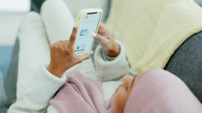 社交媒体，电话和双手，一名穆斯林妇女躺在她家客厅的沙发上，阅读头条新闻。女性通过移动技术放松，浏览和