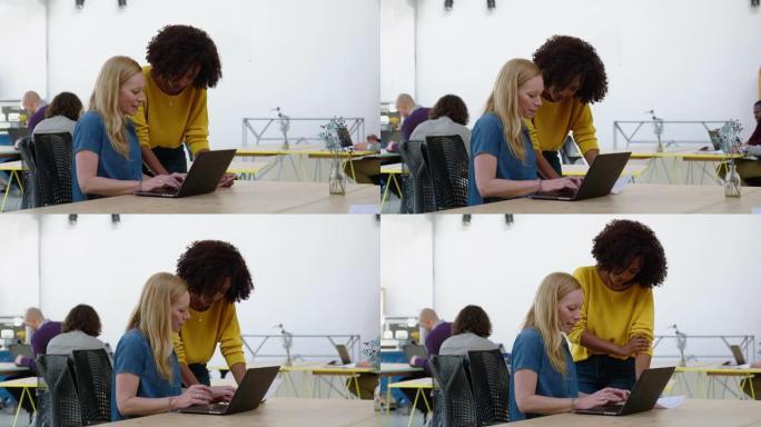 女商人与在办公桌上使用笔记本电脑的同事讨论文档