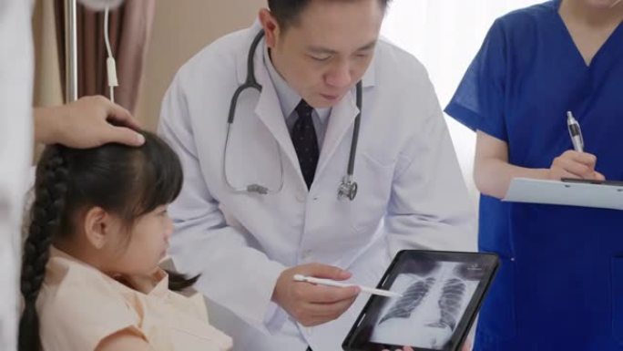 亚洲友好的医生与父母交谈，并在医院病房的平板电脑上显示x射线结果。儿童医院儿科病房。医生随访病情患者