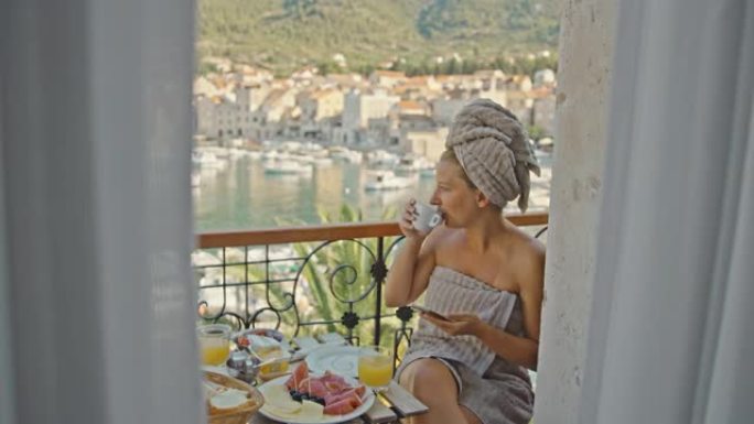 SLO MO女人在海边的阳台上吃早餐时使用手机