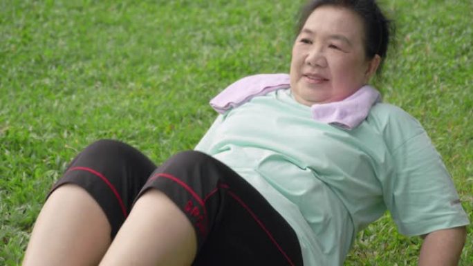 亚洲健康的高级女性在公园里做胃嘎吱嘎吱。老年女性在绿色玻璃上锻炼。早上做腹部核心运动，让老祖母在户外