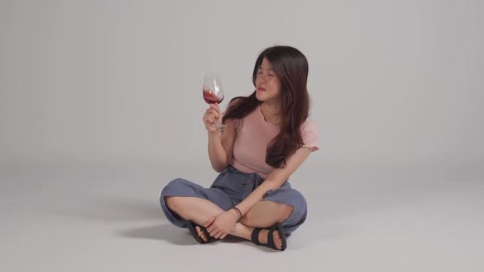 亚洲华人美女坐在地板上喝红酒享受