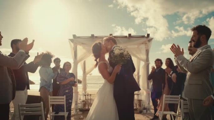 美丽的新娘和新郎在海边的海滩上户外庆祝婚礼。完美的婚姻场所，最好的多民族多元朋友在新婚夫妇身上扔花瓣