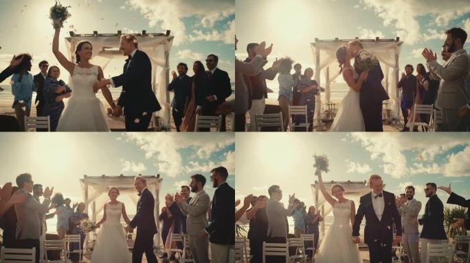 美丽的新娘和新郎在海边的海滩上户外庆祝婚礼。完美的婚姻场所，最好的多民族多元朋友在新婚夫妇身上扔花瓣