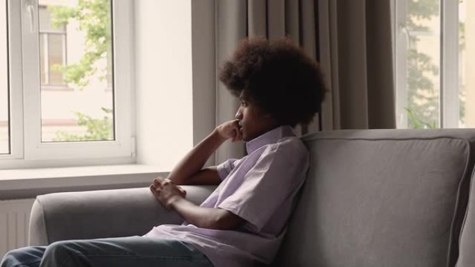 悲伤的非洲少年坐在沙发上凝视窗外