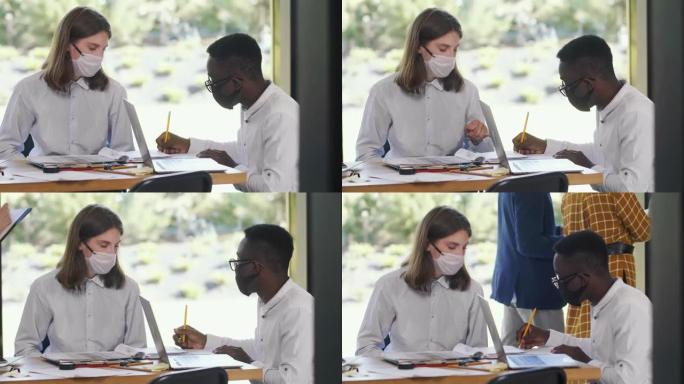 新型冠状病毒肺炎后，两名年轻快乐的多民族业务经理在办公室一起工作，戴着医用口罩。