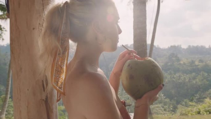 年轻的旅游女人在热带酒店度假胜地喝椰子鸡尾酒，看着美丽的丛林景色，享受天堂里异国情调的度假生活方式