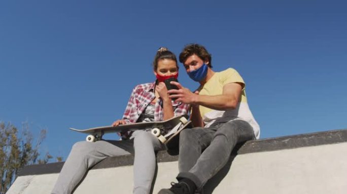 白人男女朋友戴着口罩，坐着并使用智能手机