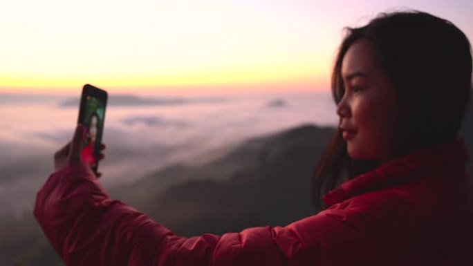 剪影年轻女子在山上用阳光和雾拍摄风景。独自旅行背包客带着相机徒步旅行。假日旅行和度假概念。