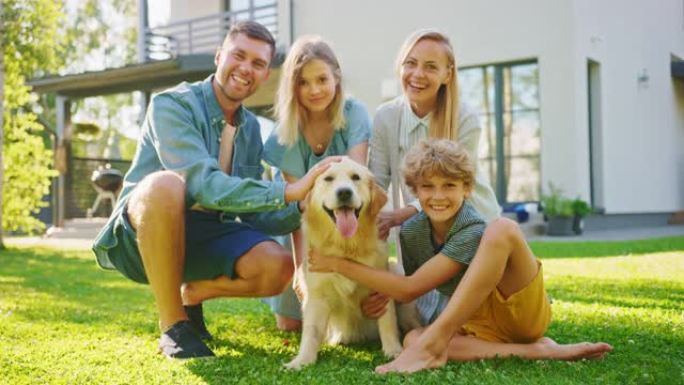 微笑的四口之家与快乐的金毛猎犬在后院草坪上摆姿势。田园诗般的家庭在避暑别墅后院与忠诚的血统狗在户外玩