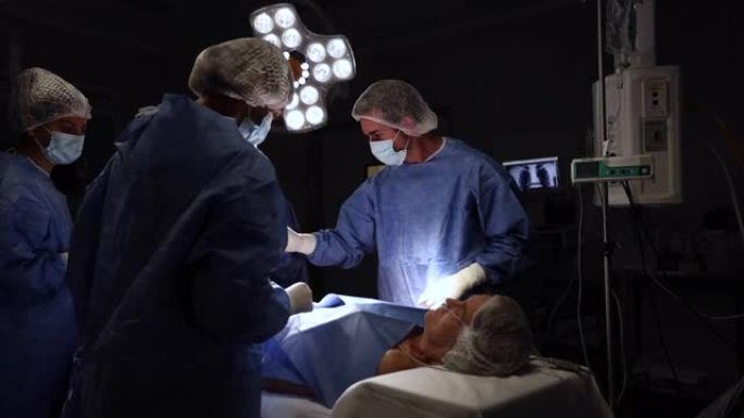 男性外科医生在仪器专家和两名实习生的协助下操作一名高级女性患者