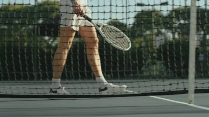 男网球运动员在网球场上蹦蹦跳跳时用球拍走路