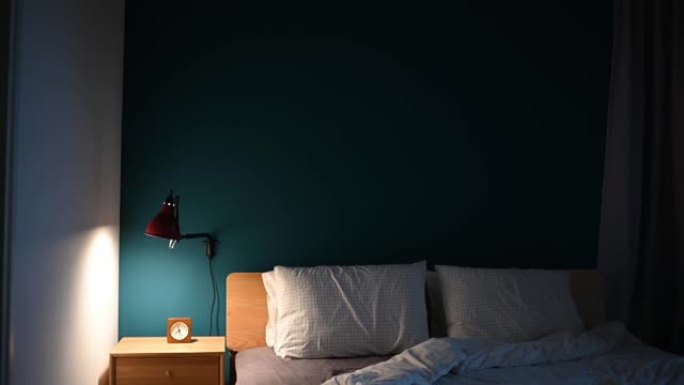 夜间卧室由电灯照明，床头柜上有时钟，床头柜上有蓝色墙壁
