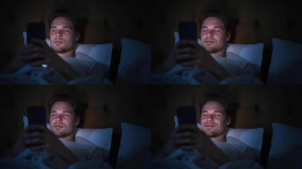 匿名男子晚上在家床上使用智能手机。帅哥浏览社交媒体，看新闻，深夜网购。专注手握手机遮脸