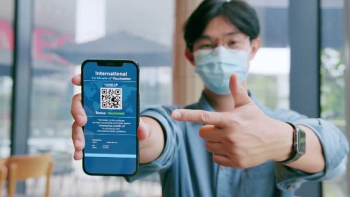 戴着口罩的亚洲男子在智能手机上展示国际新型冠状病毒肺炎疫苗接种证书。