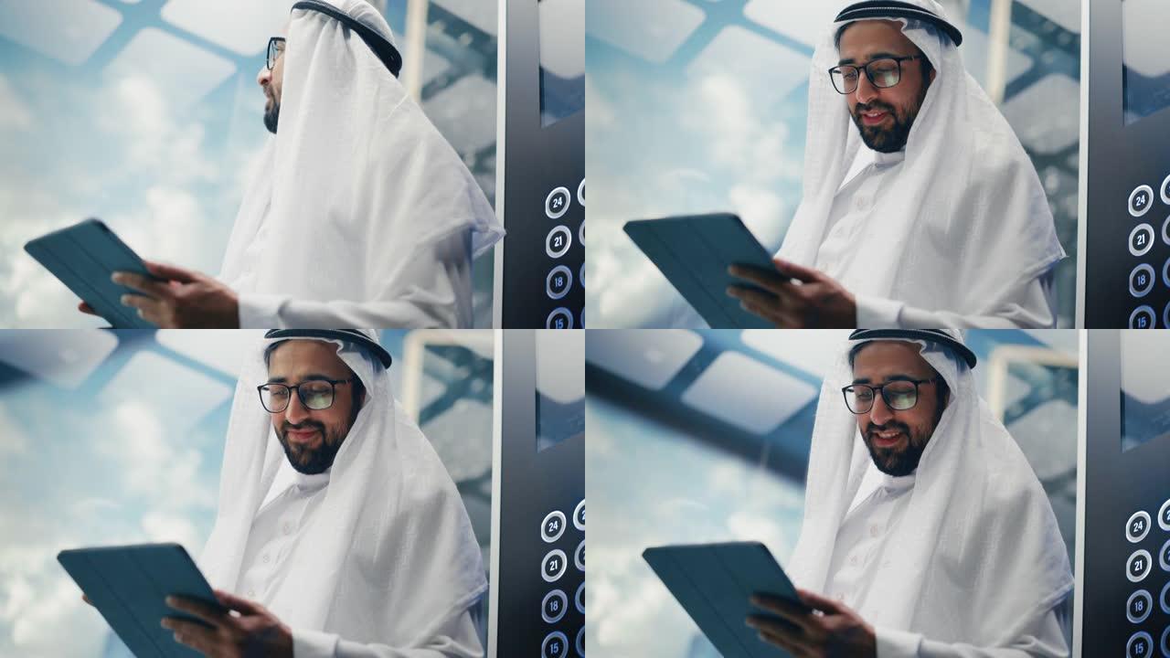 成功的穆斯林商人在传统的白色坎杜拉骑着玻璃电梯到现代商务中心的办公室。使用平板电脑的人。沙特、阿联酋