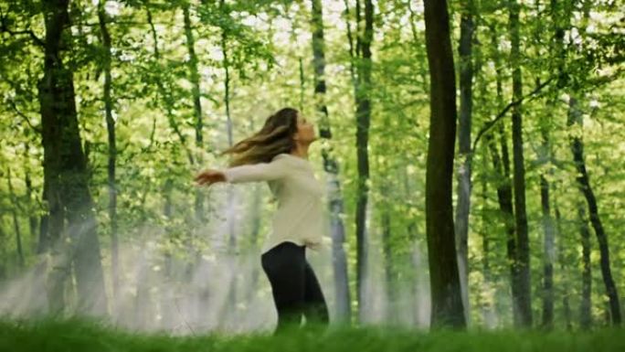 SLO MO女人在阳光明媚的森林中的绿色林间空地中旋转时享受着大自然
