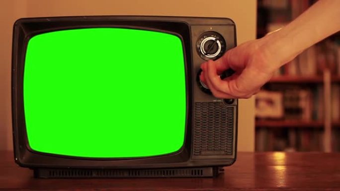 男人在带有绿色屏幕的旧电视上调节电视频道的音量。